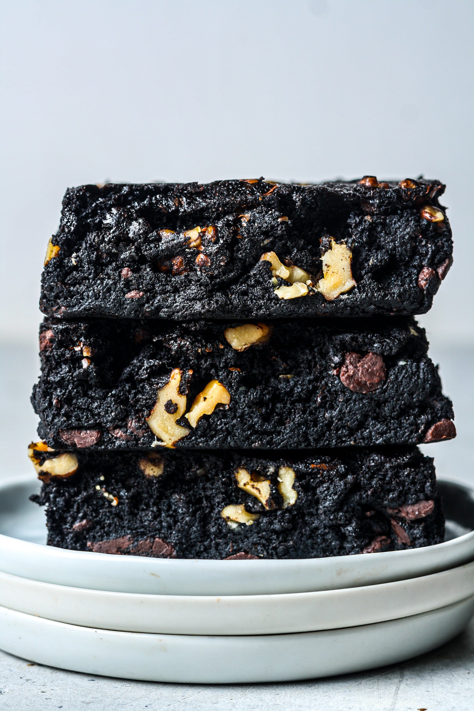 Assorted Walnut Protein Brownies from Sweet Addison's arranged on a plate with walnuts and chocolate chunks.