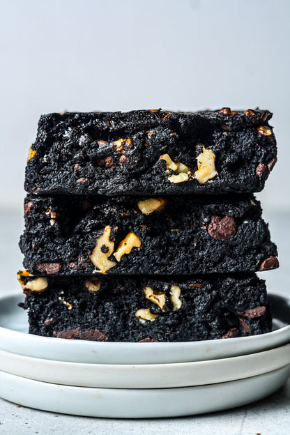 Assorted Walnut Protein Brownies from Sweet Addison's arranged on a plate with walnuts and chocolate chunks.