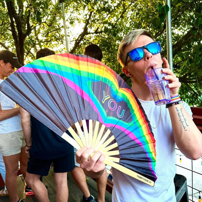 Hand fan by The Gay Fan Club featuring "Love You" design, colorful fan with vibrant patterns and a wooden handle.