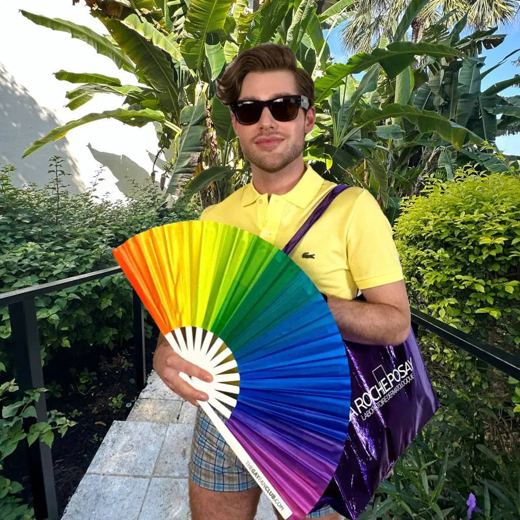 Colorful hand fan featuring rainbow stripes from The Gay Fan Club, ideal for festivals and pride celebrations.