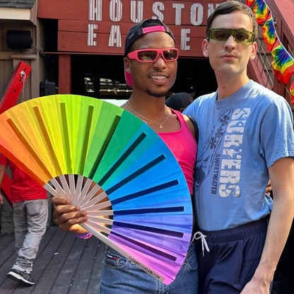 Colorful rainbow hand fan from The Gay Fan Club featuring vibrant rainbow stripes for pride celebrations and events.