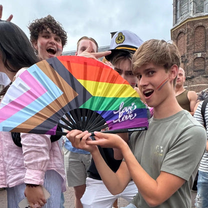 Hand fan featuring a vibrant rainbow Pride flag design from The Gay Fan Club, showcasing colorful stripes and a compact size.