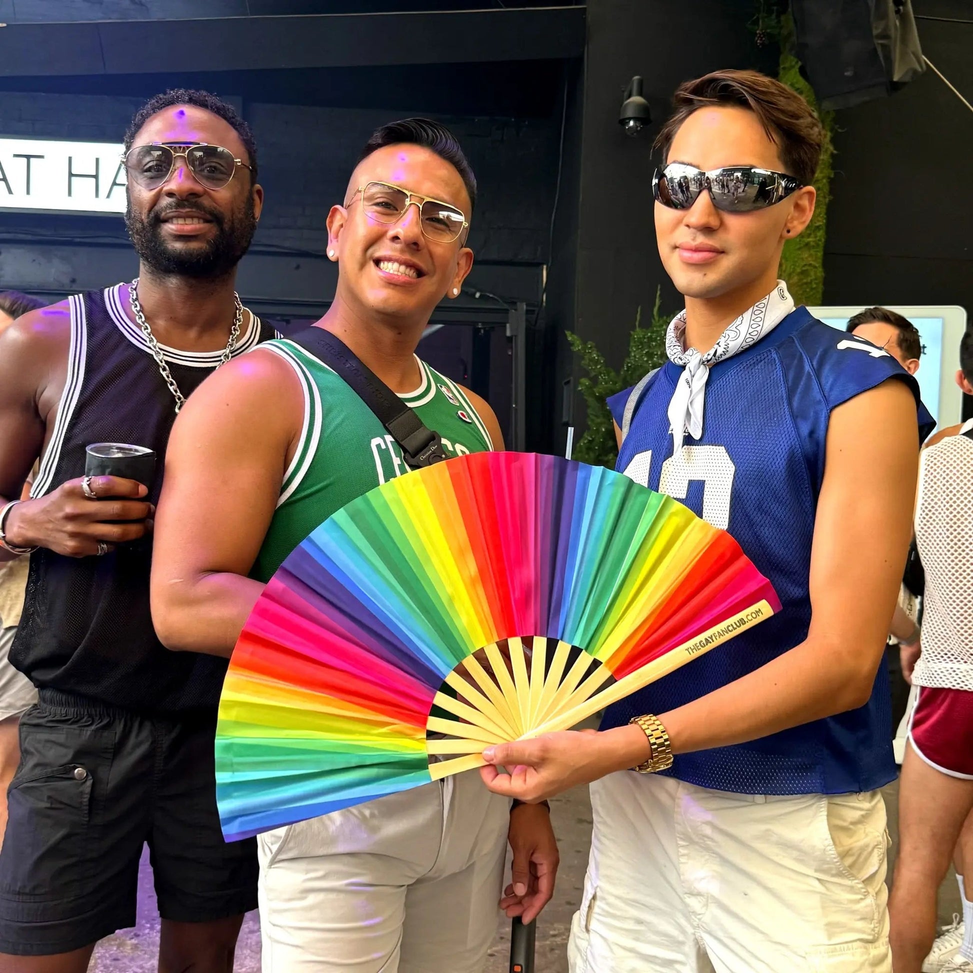 Rainbow folding hand fan by The Gay Fan Club featuring vibrant rainbow-colored fabric and a folding wooden handle.