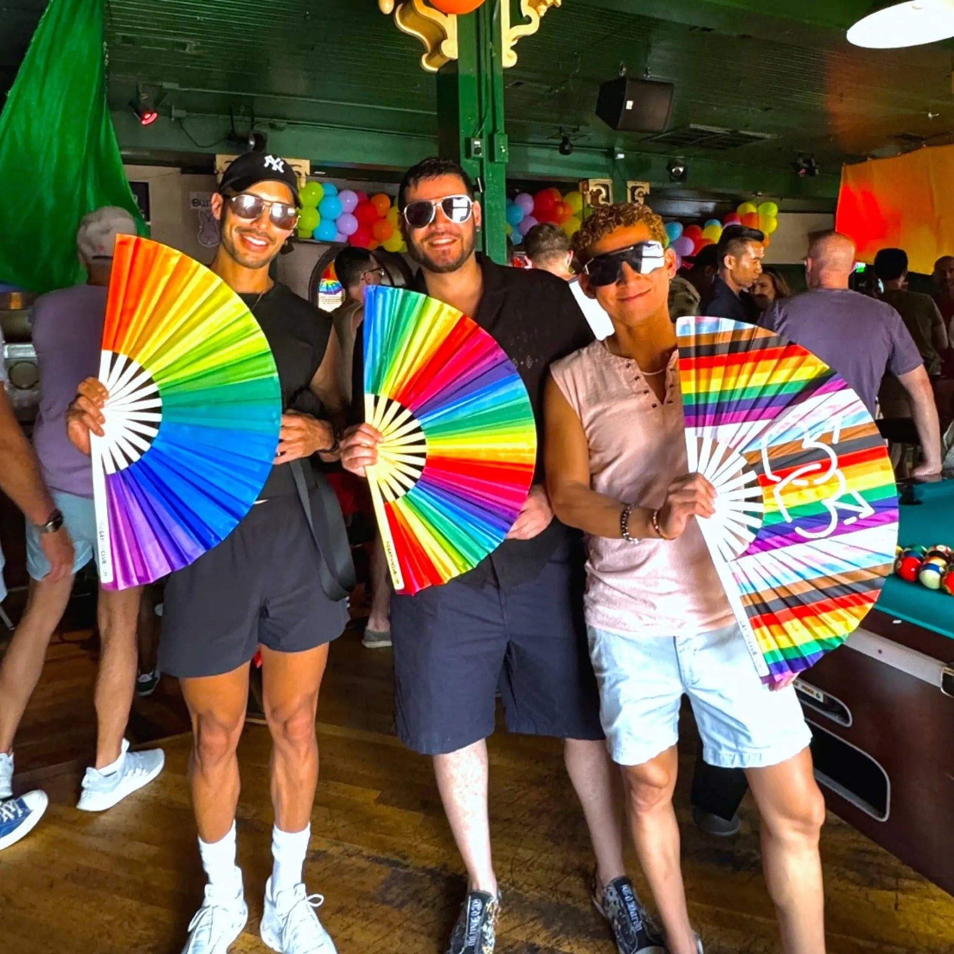 Rainbow folding hand fan by The Gay Fan Club, featuring vibrant rainbow colors and a compact, foldable design.