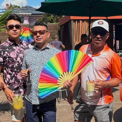 Rainbow folding hand fan by The Gay Fan Club with vibrant rainbow-colored fabric and compact folding design.