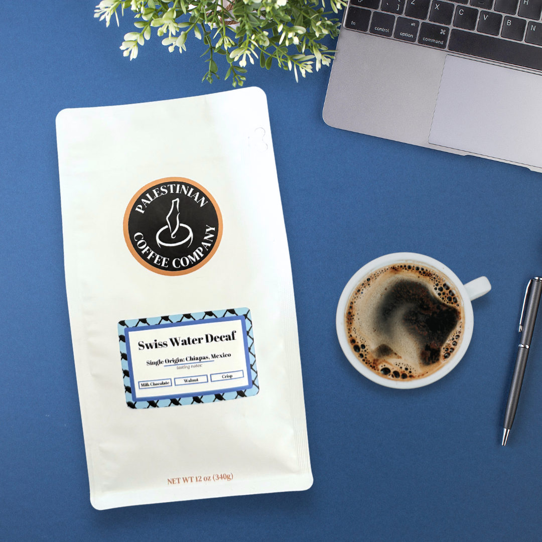 Whole bean Swiss Water decaf coffee by The Palestinian Coffee Company, showcasing dark roasted beans in a natural setting.
