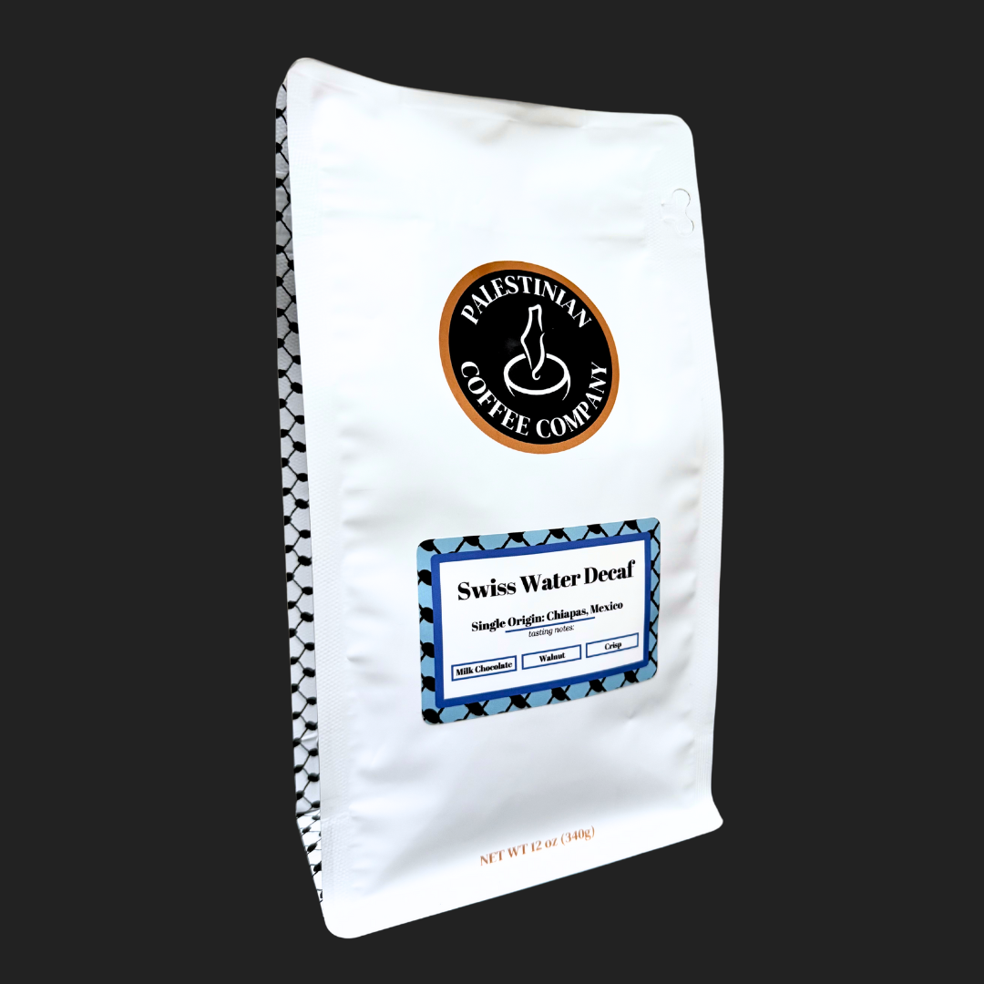 Whole bean Swiss Water Decaf Coffee by The Palestinian Coffee Company, showing dark roasted beans in a natural setting.